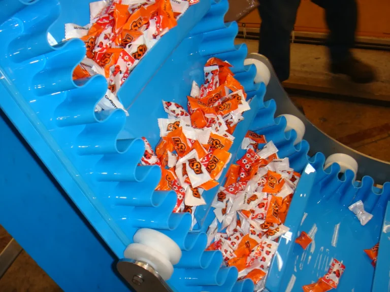 Cleated belt with sidewalls carrying wrapped sweets on an incline conveyor