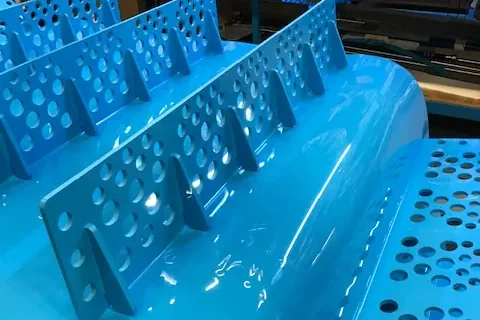 Perforated cleats welded to a blue thermoplastic belt in Volta's fabrication workshop