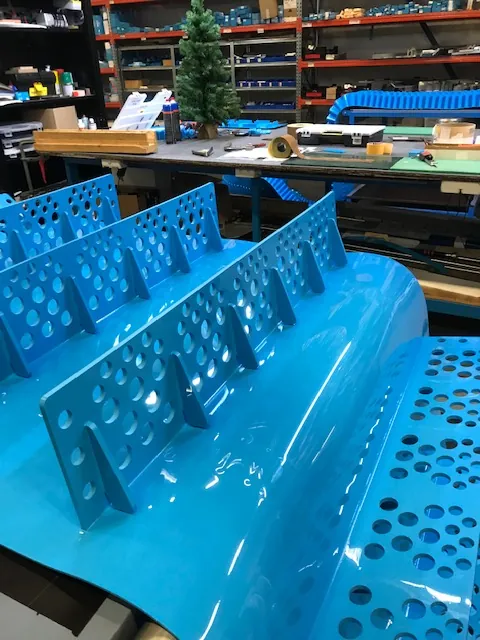Perforated cleats welded to a blue thermoplastic belt in Volta's fabrication workshop